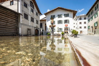 Der Holzbrunnen von Valendas – mit 15'000 Litern der grösste Holzbrunnen Europas, geschmückt mit der eindrucksvollen Brunnen-Nixe (Foto: © Autor: Jolanda Rechsteiner, Quelle: Surselva Tourismus AG) Der grosse Holzbrunnen von Valendas mit der Brunnen-Nixe, umgeben von historischer Dorfkulisse