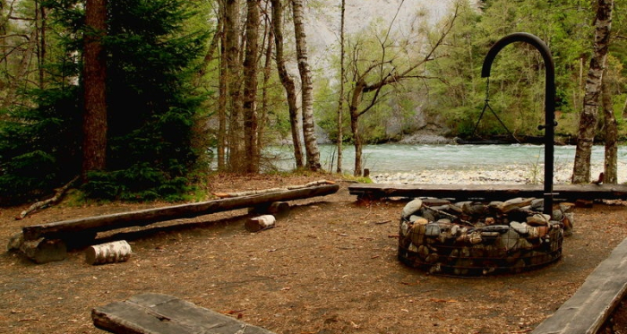 Grillstelle am Rhein mit Holzbänkli rundherum und Wald.