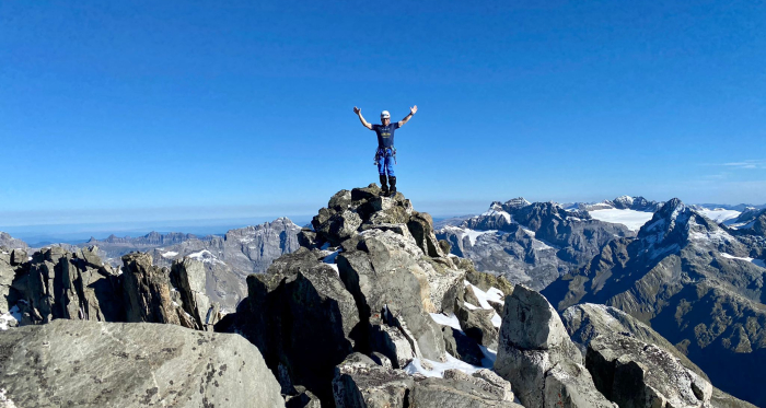 Glücksmoment auf dem Gipfel – David Baer auf dem Oberalpstock Bergsteiger mit erhobenen Armen auf felsigem Gipfel des Oberalpstocks