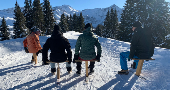 Schneevergnügen und gute Laune – unterwegs mit Marc Steiner Vier Männer sitzen auf Holzschlitten bei winterlicher Berglandschaft