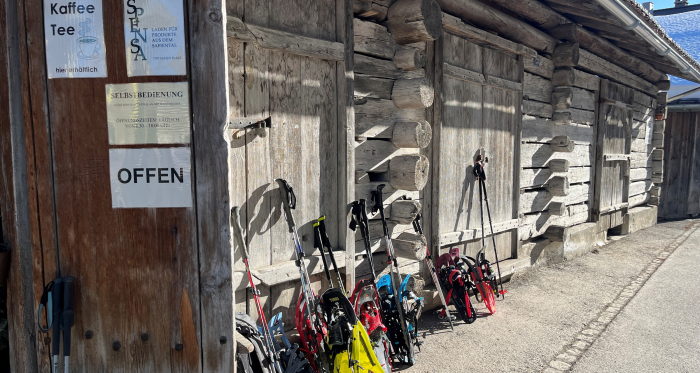 Einkehr mal anders – Schneeschuhtour mit Zwischenstopp bei der Spensa im Safiental Schneeschuhe und Stöcke vor Selbstbedienungsladen Spensa in traditionellem Holzhaus