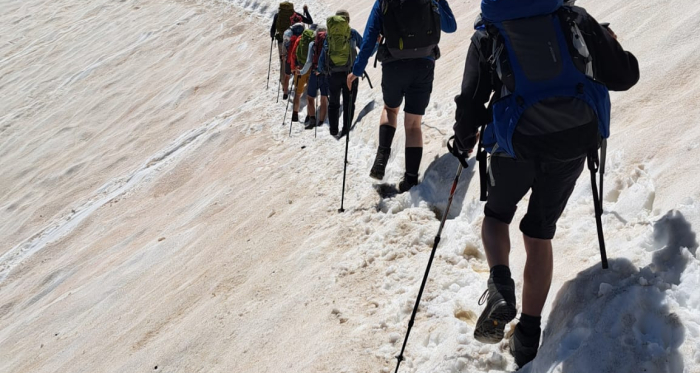 Sicher geführt über Schnee und Stein – Susanne begleitet Touren bis T4 mit Umsicht und Begeisterung Wandergruppe überquert ein Schneefeld unter blauem Himmel