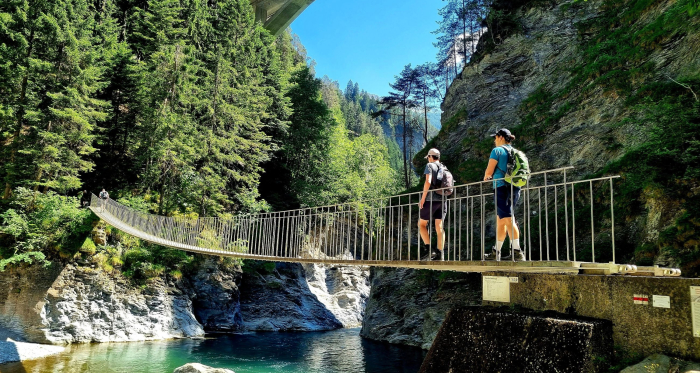 Zwei Personen überqueren eine Hängebrücke in der Viamala-Schlucht umgeben von hohen Felswänden