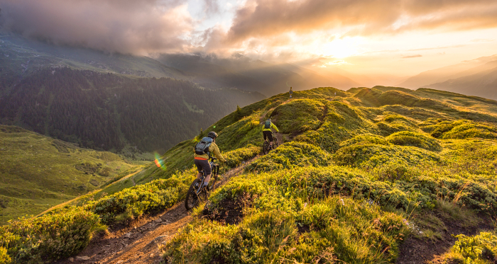 Zwei Mountainbiker fahren bei Sonnenuntergang über einen Gratweg