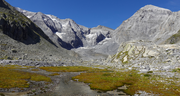 Berglandschaft mit einem Flussbett, umgeben von Geröll und Felsformationen, die zu Gletschern aufsteigen