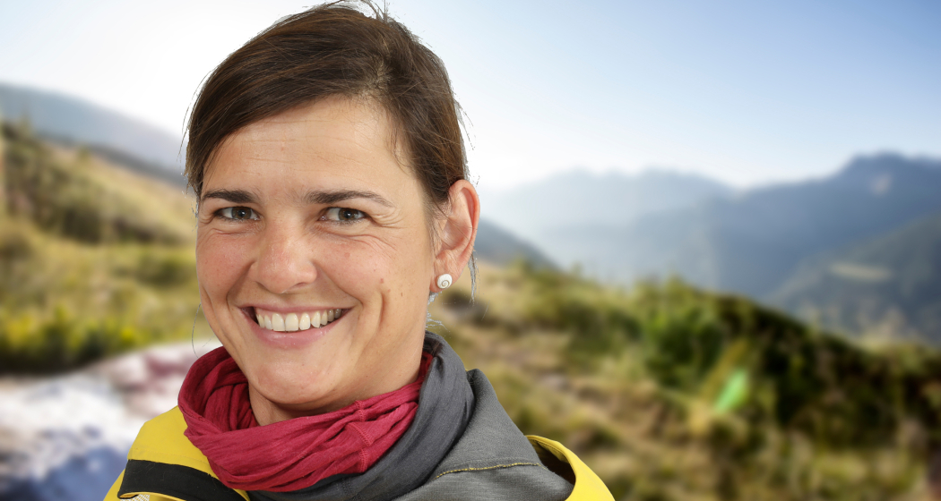 Susanne Kern ist mit Herz und Humor in den Bündner Bergen unterwegs – Ihre Wanderleiterin für besondere Erlebnisse Porträt von Wanderleiterin Susanne Kern vor einer verschwommenen Berglandschaft