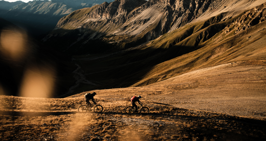 Ein Paar fährt auf Mountainbikes einen Trail in Graubünden hinunter