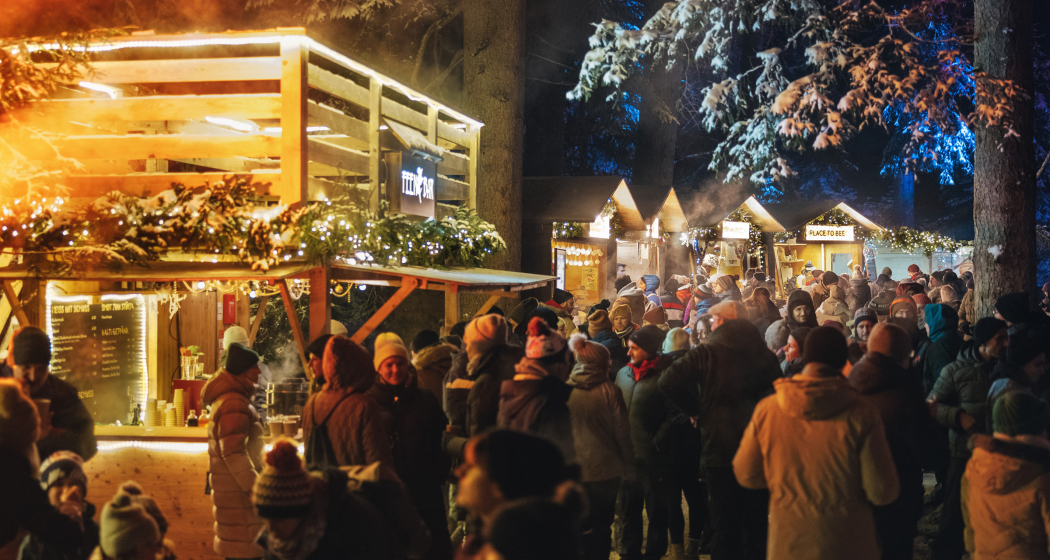Besucherinnen und Besucher flanieren zwischen beleuchteten Marktständen im winterlichen Zauberwald Lenzerheide