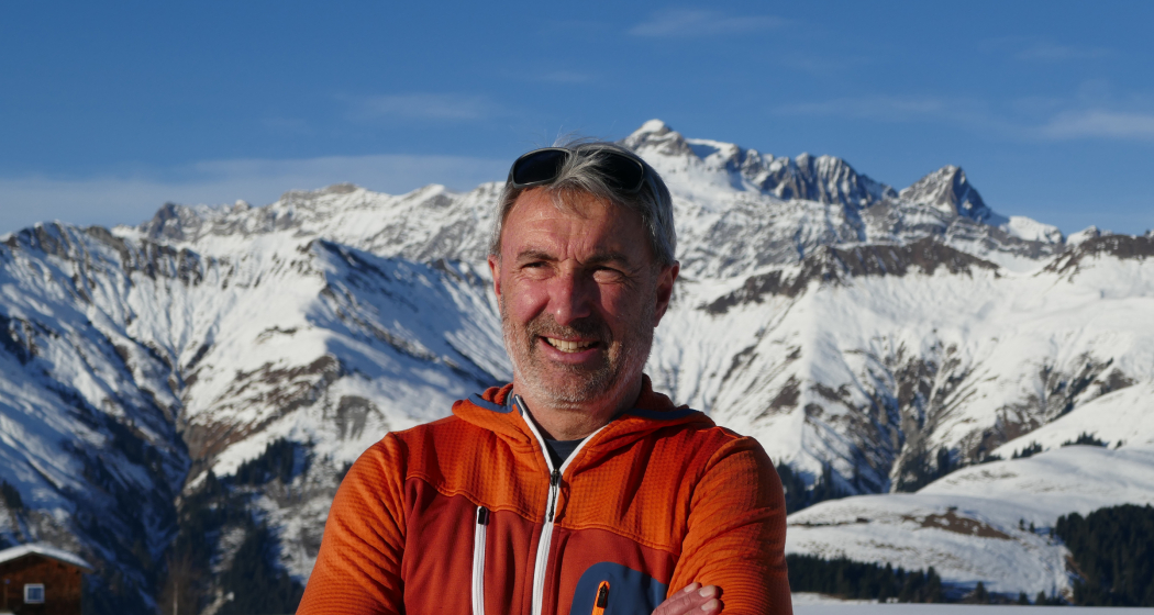 Porträt von Wanderleiter Cyrill Locher in orangefarbener Outdoorjacke vor verschneiten Berggipfeln in Graubünden