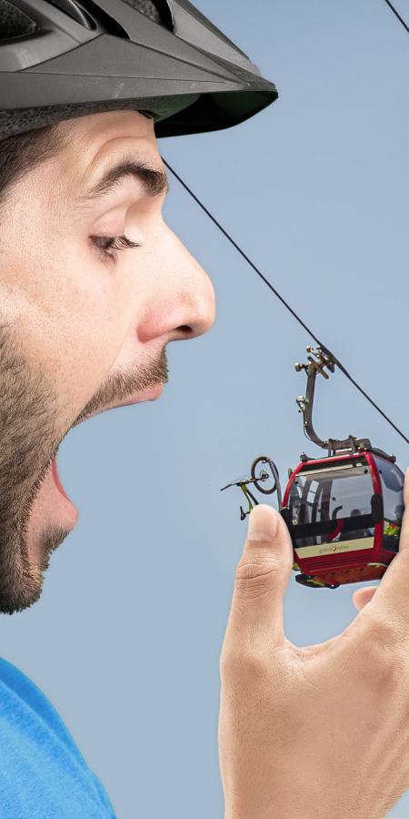 Ein übergrosser Mountainbiker beisst in die Gondel einer Bergbahn