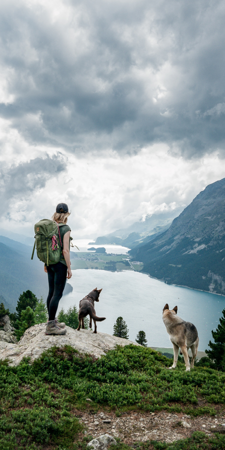 Eine Wanderin geniesst mit ihren beiden Hunden die Aussicht auf die Oberengadiner Seenplatte