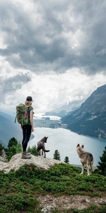 Eine Wanderin geniesst mit ihren beiden Hunden die Aussicht auf die Oberengadiner Seenplatte