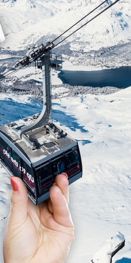 Eine übergrosse Skifahrerin in voller Montur beisst spielerisch in eine Gondel einer Bergbahn