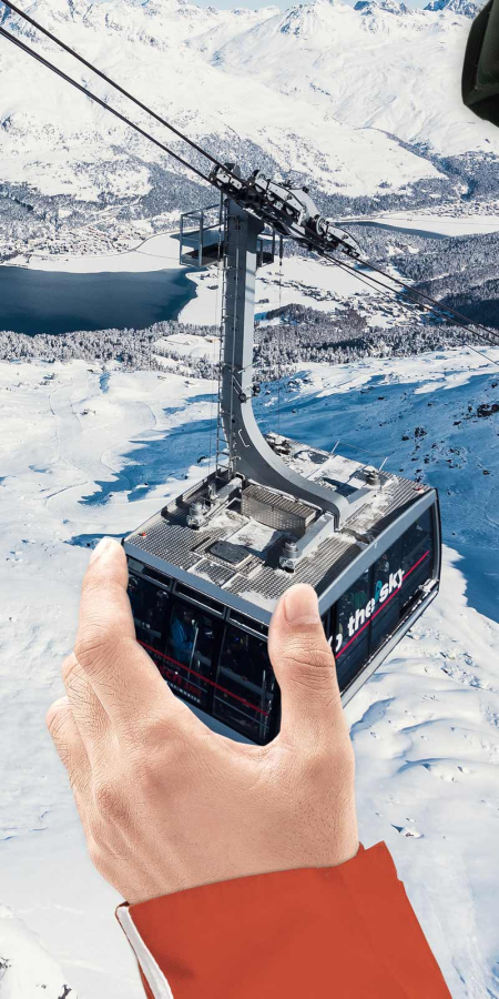 Ein übergrosser Skifahrer in voller Montur beisst spielerisch in eine Gondel einer Bergbahn