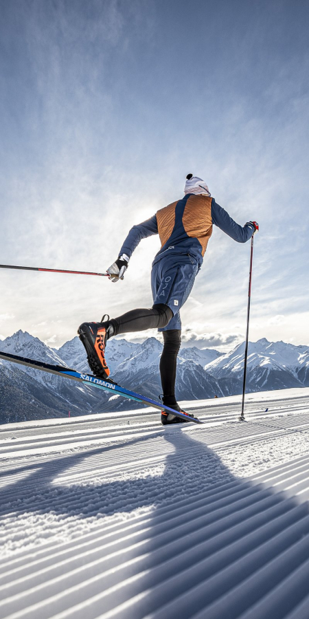 Langlaufen im Unterengadin: Traumhafte Loipen mit beeindruckender Bergkulisse (Foto: © Tourismus Engadin Scuol Samnaun Val Müstair AG (TESSVM) / Andrea Badrutt) Ein Langläufer auf einer verschneiten Loipe im Unterengadin, im Hintergrund ein beeindruckendes Bergpanorama