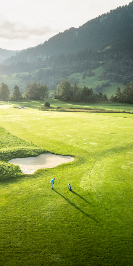 Golfspieler auf dem Golfplatz Buna Vista in Sagogn mit Blick auf das sonnenbeschienene Tal und umliegende Berge