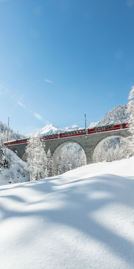 Bernina Express auf dem Albulaviadukt in tief verschneiter Winterlandschaft