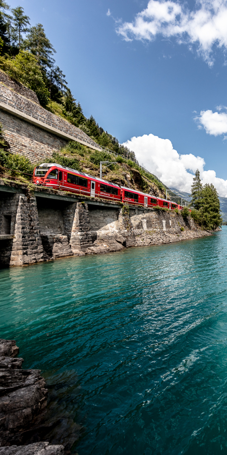 Regionalzug der Rhätischen Bahn am Lago di Poschiavo an einem sonnigen Sommertag