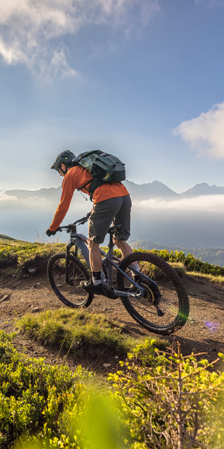 Goldenes Licht, grüne Hügel und pure Trailfreude in Disentis Sedrun (Foto: © WOM Medien) Zwei Mountainbiker fahren bei Sonnenaufgang auf einem flowigen Singletrail durch die grüne Berglandschaft in der Ferienregion Disentis Sedrun