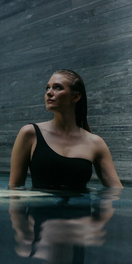 Jeune femme en maillot de bain noir dans l’espace intérieur des thermes 7132 à Vals, entourée de murs en quartzite de Vals