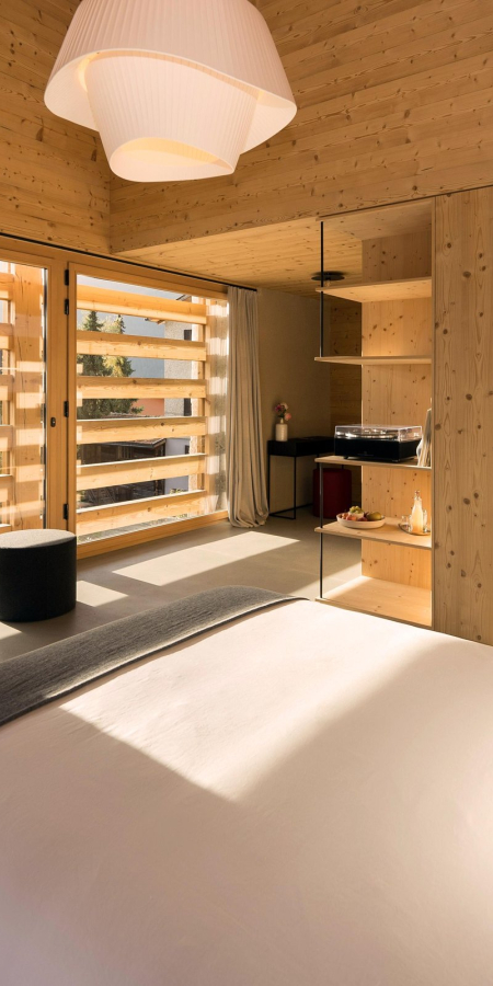 Chambre confortable de la Casa Giovanoli avec des parois en bois et vue sur le balcon ensoleillé