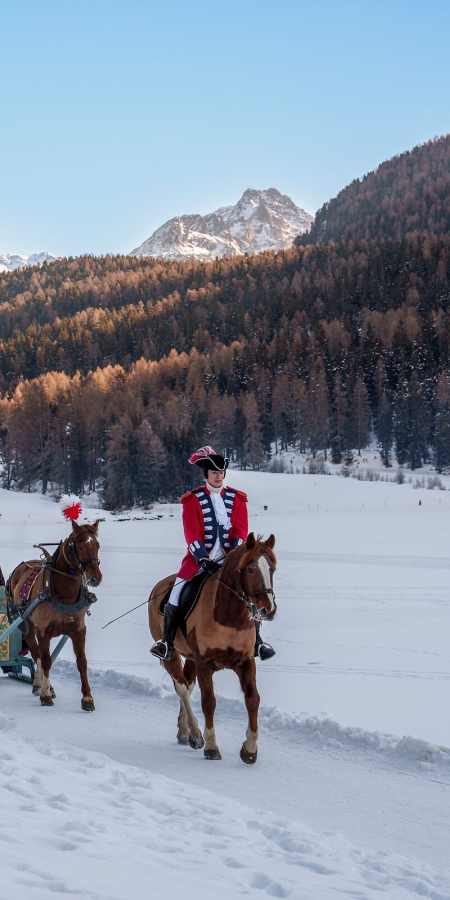 Schlitteda im Oberengadin mit Pferdeschlittenzug durch verschneite Landschaft vor Bergkulisse