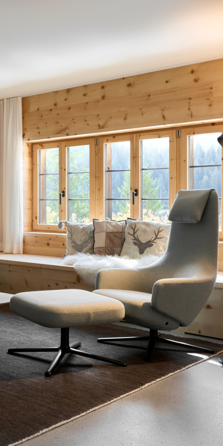 Fauteuil moderne avec repose-pieds devant un banc de fenêtre en bois dans un appartement de la Casa Mulania à Laax