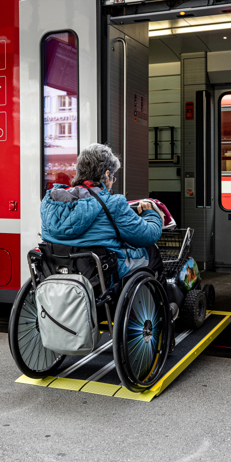 Person in a wheelchair boards a train of the Rhaetian Railway via a ramp