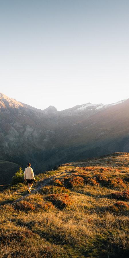 Wanderer auf Alpweide bei Sonnenaufgang mit Bergpanorama in der Viamala, Tschappina Glaser Grat.