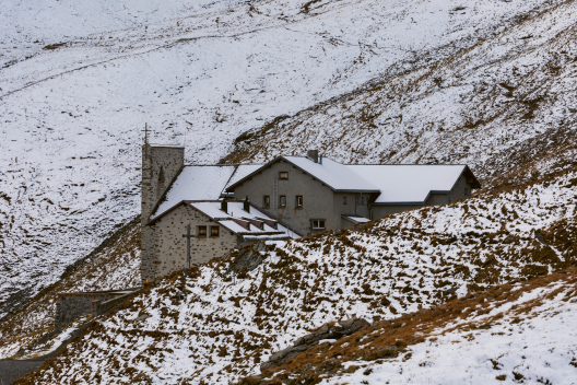 Steinhaus mit Kirche in schneebedeckter Berglandschaft im Herbst. (Foto: © Nico Schaerer) Steinhaus mit Kirche in schneebedeckter Berglandschaft im Herbst.
