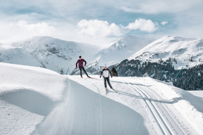 Langlaufen auf der Capfedersloipe in Parpan: Sport und Natur in perfekter Harmonie auf der Lenzerheide (Foto: © Hannah Bichay/Ferienregion Lenzerheide) Ein Paar gleitet sportlich auf der Capfedersloipe in Parpan entlang, umgeben von tief verschneiten Bergen und einer atemberaubenden Winterlandschaft