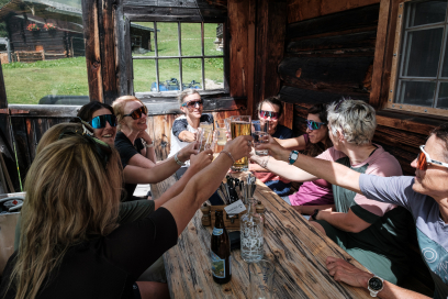Eine Gruppe von Mountainbikerinnen stösst in einer Berghütte mit Getränken an und geniesst die gemeinsame Zeit