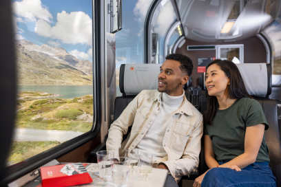À bord du Bernina Express – voyage panoramique avec vue sur le Lago Bianco (Photo : © Chemins de fer rhétiques / Nicola Pitaro) Deux voyageurs à bord du Bernina Express regardent par la fenêtre panoramique le Lago Bianco et les montagnes grisonnes