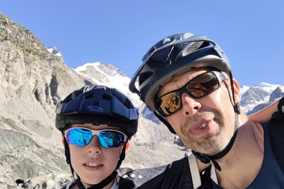 Vater und Sohn beim Mountainbiken in den Alpen Mann und Junge mit Helmen vor alpiner Berglandschaft mit Schnee und blauem Himmel