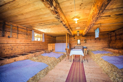 Innenraum des Maiensäss Molas Sot im Val Surses: gemütlicher Stall mit Strohlagerplätzen, Holzwänden und einfachem Aufenthaltsbereich mit Tisch und Stühlen