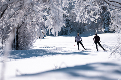 Durch verschneite Wälder gleiten und die Stille geniessen – Langlaufen in Graubünden bedeutet pure Winteridylle (Foto: © Filip Zuan) Zwei Langläuferinnen auf verschneiter Waldloipe zwischen vereisten Bäumen