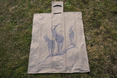Beige Picknickdecke mit Tragegriff liegt auf einer Wiese. Darauf sind drei Steinböcke und der Schriftzug Graubünden abgebildet.