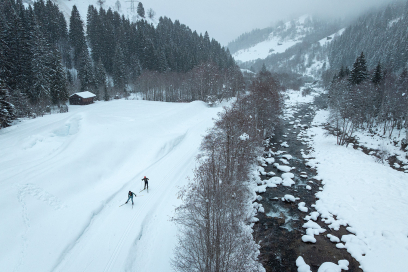 Zwei Personen beim Langlaufen auf einer Loipe am Bachufer in Disentis.