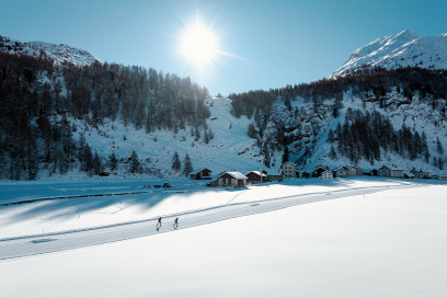 Zwei Personen auf der schneebedeckten Langlaufloipe vor verschneiten Bergen und Chalets
