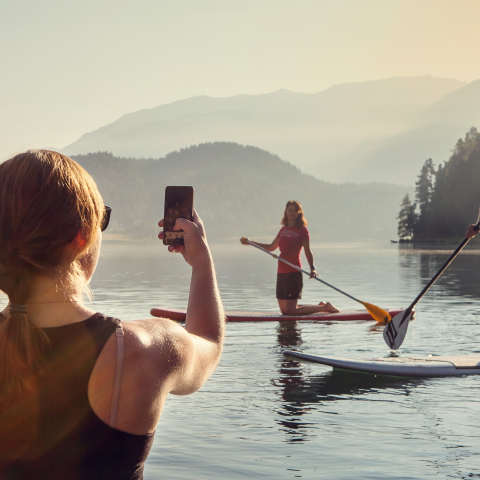 Lake St. Moritz is ideal for stand-up paddling (Photo: © Engadin Tourismus AG / Filip Zuan) A woman uses a smartphone to photograph a man and a woman on boards for stand-up paddling on Lake St. Moritz