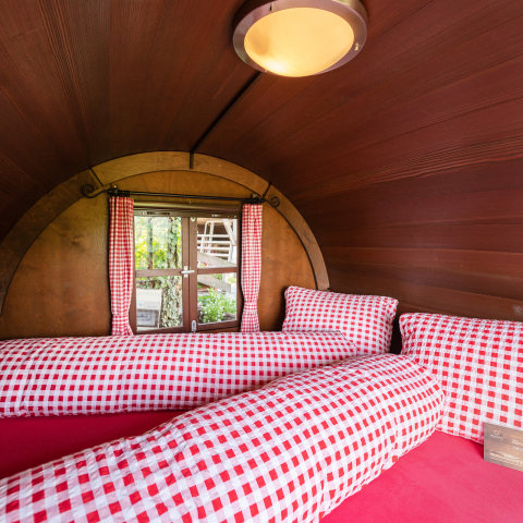 Gemütlicher Innenraum eines Schlaf-Fasses mit kariertem Bettbezug und Holzverkleidung
