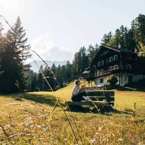 Der Hof Zuort im Unterengadin ist der perfekte Rückzugsort (Foto: © Sommertage) Bloggerin Katharina Werni liest auf einer Bank vor dem Hof Zuort in einem Buch