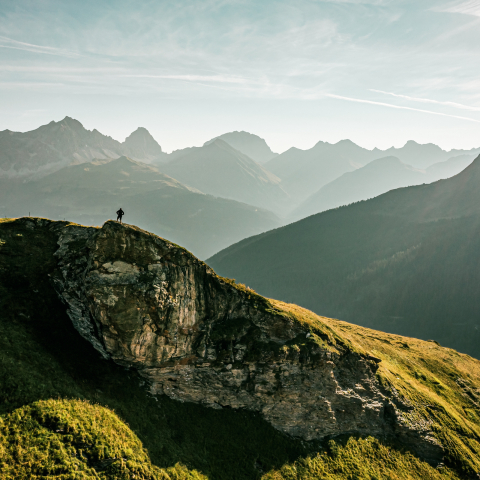 Fadri Arpagaus inmitten der Bergwelt von Radons (Foto: © Schweiz Tourismus / Christian Meixner) Fadri Arpagaus steht auf einem Felsen inmitten der Bergwelt von Radons und schaut sich denn Sonnenaufgang an