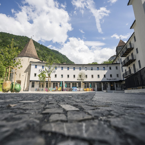 Bogentrakt Hostel Chur (Foto: © Marco Hartmann) Aussenansicht des Bogentrakt Hostels im Sennhof Chur mit historischem Rundturm heller Fassade und bunter Terrasse vor grünem Berghintergrund