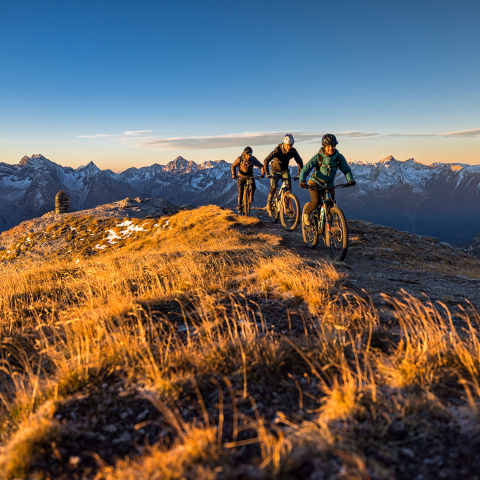 Mountainbiker bei Sonnenaufgang auf einem Grat im herbstlichen Graubünden