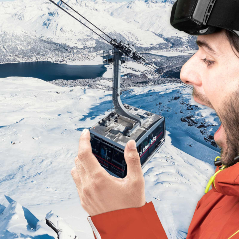 Ein übergrosser Skifahrer in voller Montur beisst spielerisch in eine Gondel einer Bergbahn