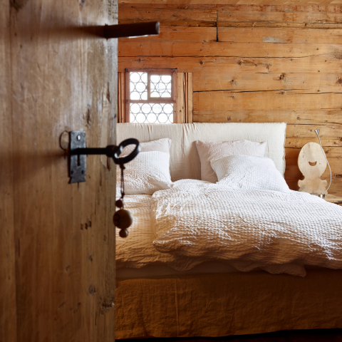 Nühus B&B im Safiental (Foto: © Graubünden Ferien / Stefan Schlumpf) Blick durch die halboffene Holztür eines Gästezimmers mit Doppelbett im Nühus B&B