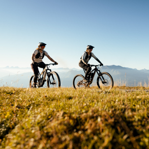 Mountainbiken mit Panoramablick – unterwegs in der eindrucksvollen Berglandschaft Graubündens (Foto: © Schweiz Tourismus) Anita und Caro Gehrig – zwei Mountainbike-Profis – fahren auf einem sonnigen Berghang mit weitem Alpenpanorama im Hintergrund