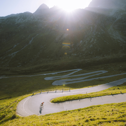 Kurve für Kurve über den Splügenpass (Foto: © Alex Strohl Photography) Rennradfahrer in einer Haarnadelkurve auf der autofreien Passstrasse am Splügenpass