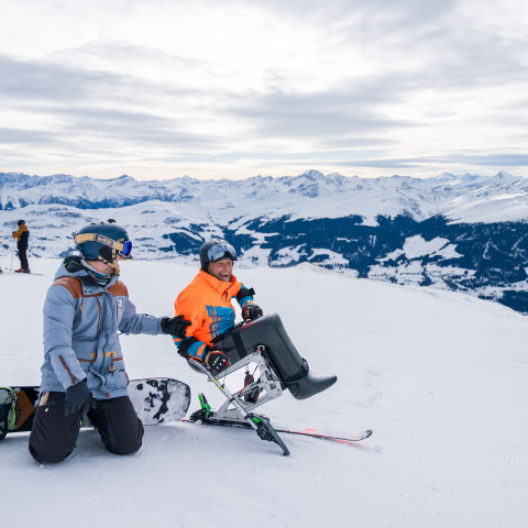 Zwei Wintersportler auf einem verschneiten Berg, einer davon im Monoski.